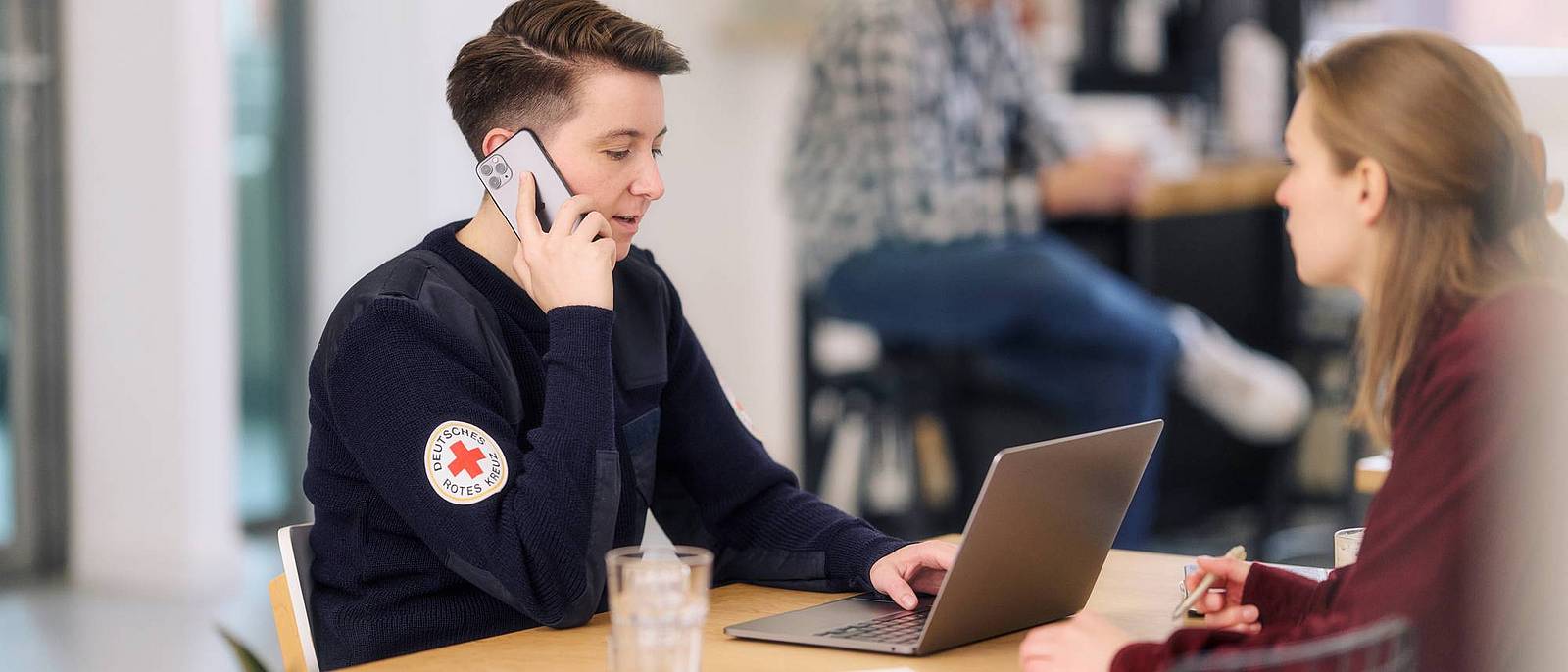 Eine telefonierende Frau sitzt an einem Tisch und arbeitet mit einem Laptop