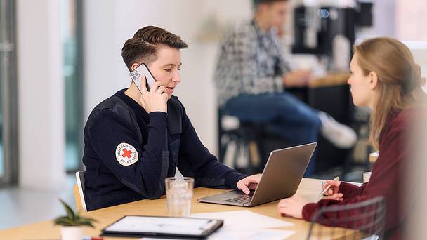 Eine telefonierende Frau sitzt an einem Tisch und arbeitet mit einem Laptop